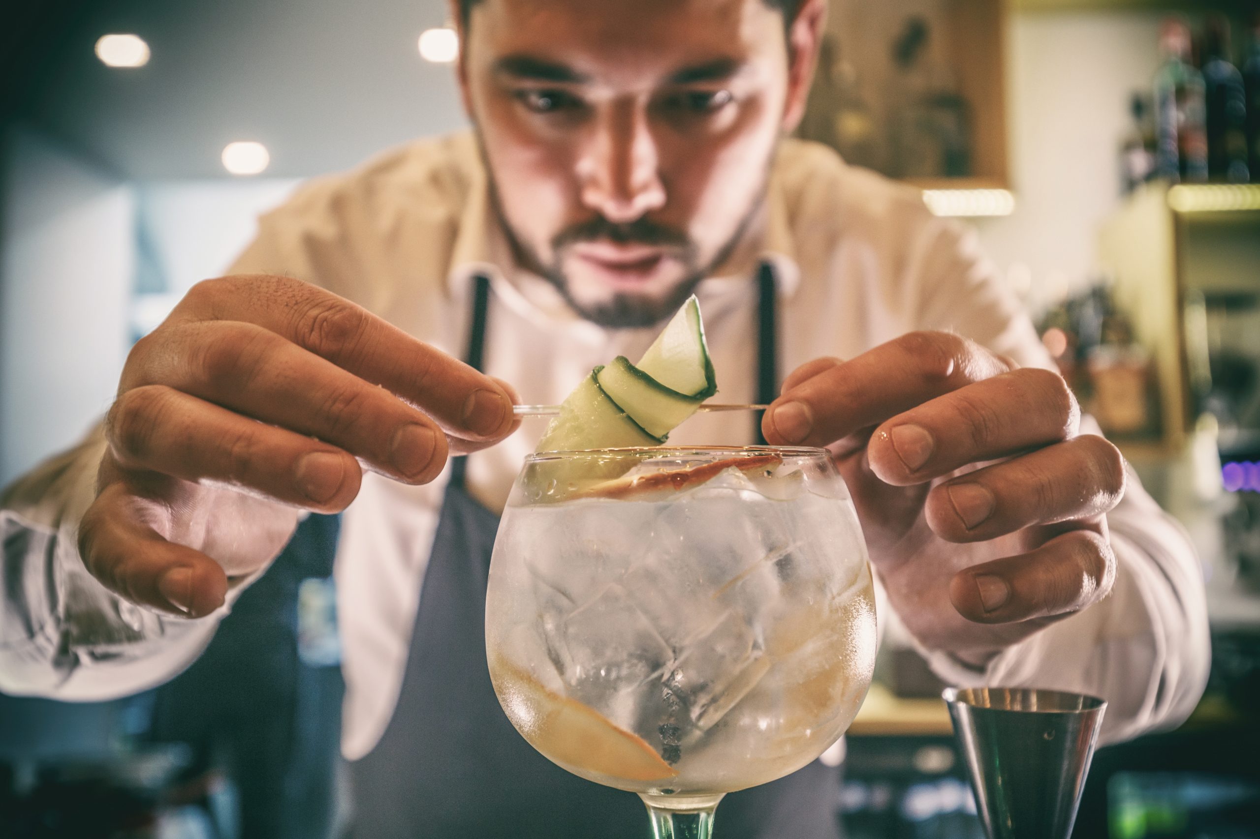 Expert barman is decorating cocktail with cucumber